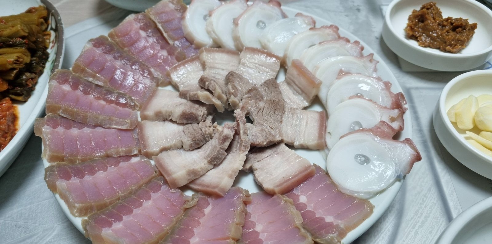 흰 접시에 홍어와 돼지 수육, 문어를 둘러 담은 모습 — 왼쪽에 김치, 오른쪽 위에 막장과 깐마늘
