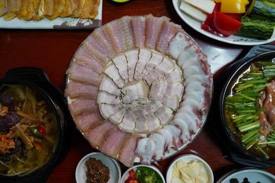 나무 상 위 접시 — 둘레에 홍어, 가운데 돼지 수육, 오른쪽에 문어